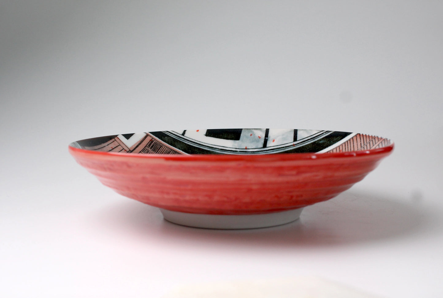Shallow plate with read body on the outside and a geisha's house facade on the inside of the bowl