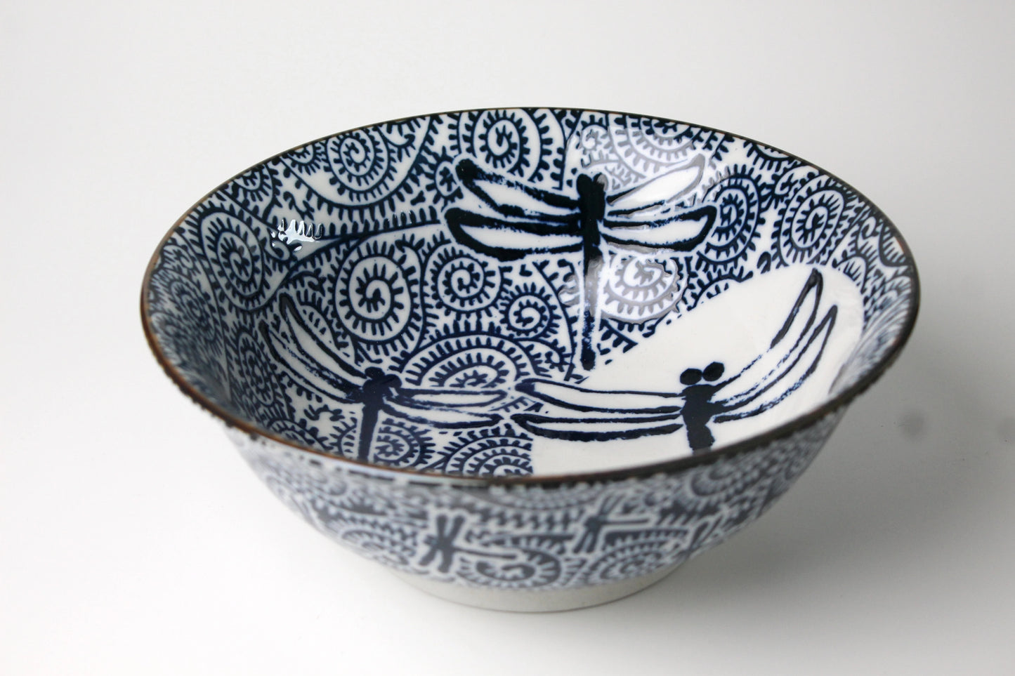 Ceramic ramen bowl featuring a blue-and-white dragonfly design and intricate swirling patterns on a white background.