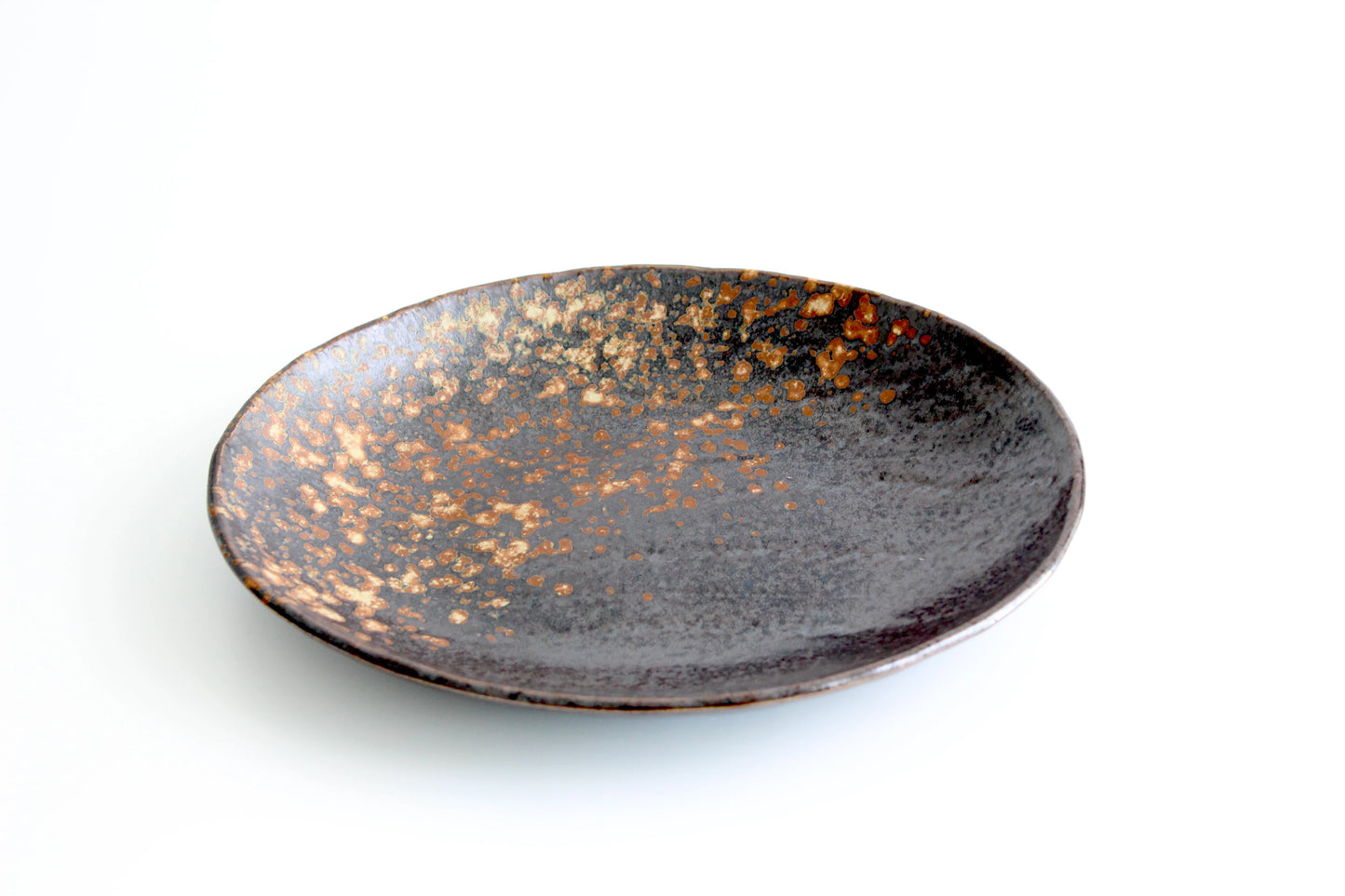 Oval ceramic plate with a comet-inspired speckled finish and gently raised, bowl-like walls, combining the elegance of a plate with the practicality of a bowl.