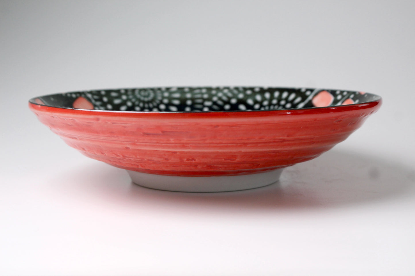 The outside body of this shallow plate is red in color. A bit of the inside design can be seen. The inside shows back sky with fireworks.