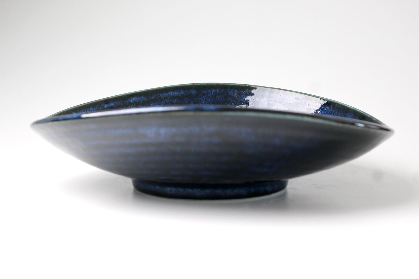Outside of a shallow plate with high walls folded inward with midnight blue glossy finish.