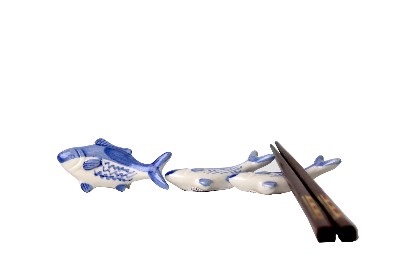 A set of ceramic tuna-shaped spoon rests in blue and white, accompanied by wooden chopsticks, displayed on a white surface.