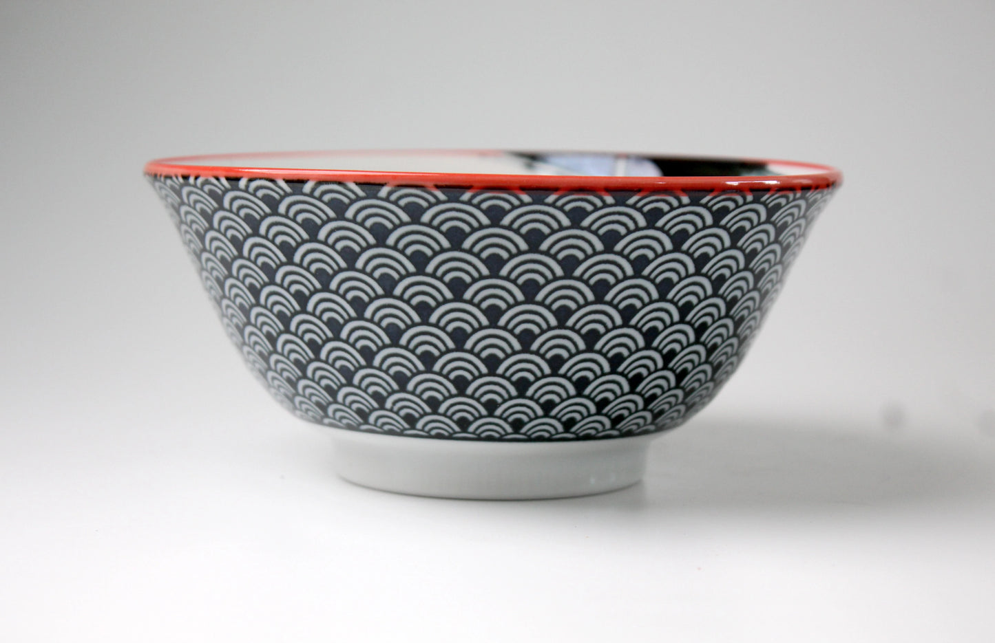 Side view of a black ceramic ramen bowl adorned with white wave patterns and a contrasting red rim