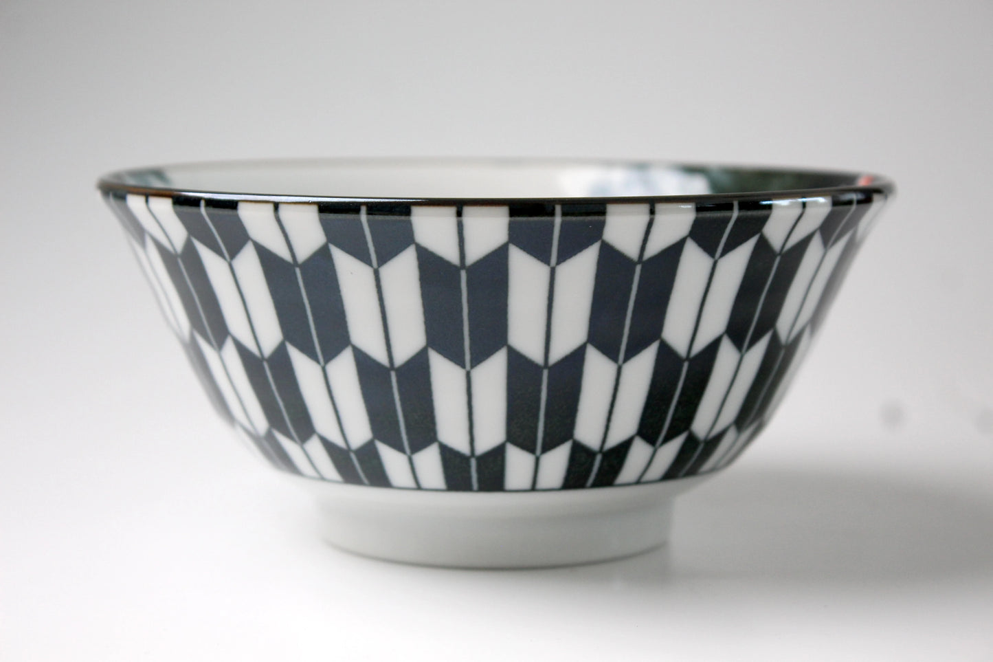 Side view of a black-and-white ceramic ramen bowl with a bold, chevron-inspired geometric pattern.