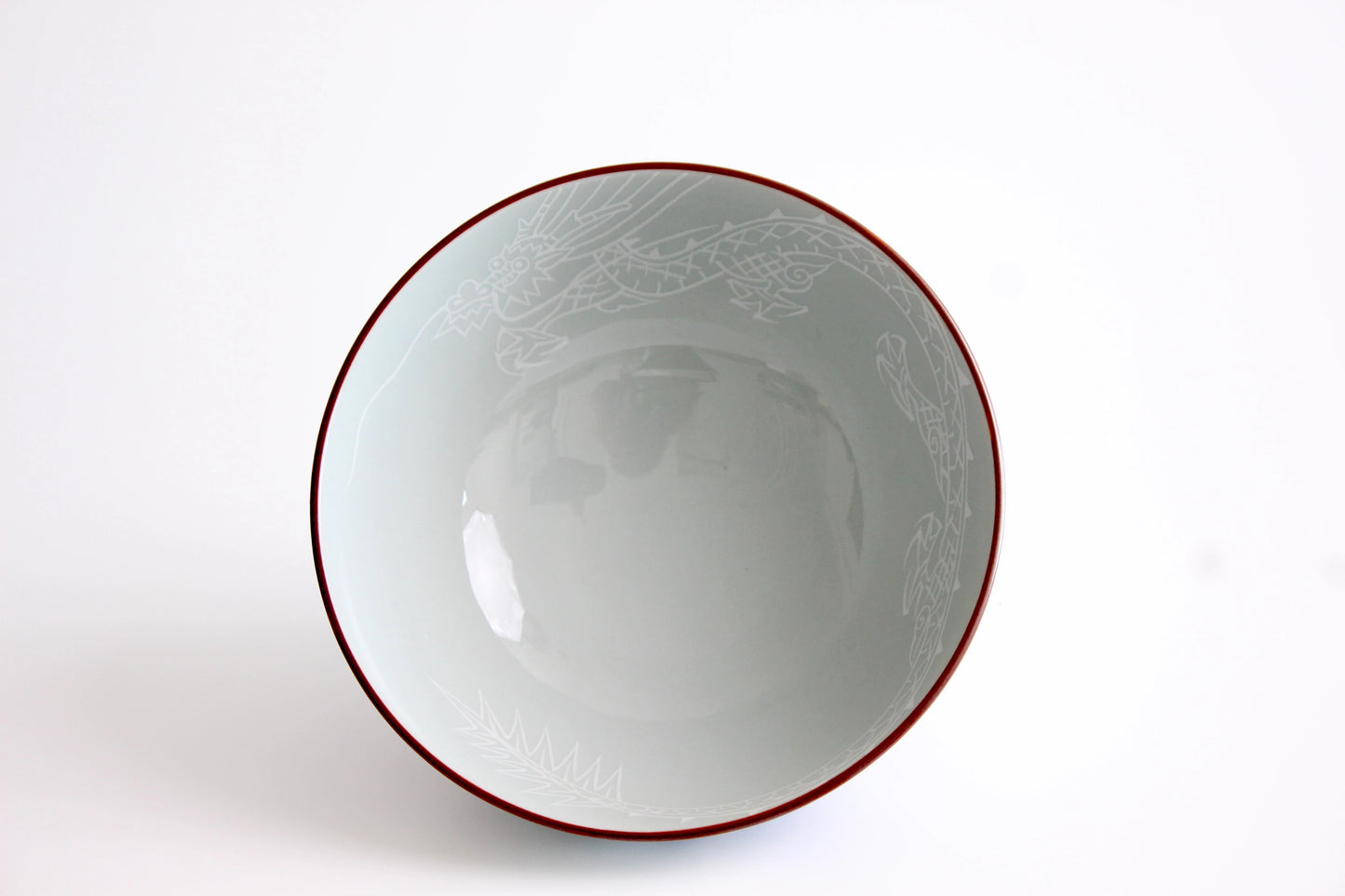 A top-view of a handcrafted porcelain rice bowl featuring an etched dragon design along the inner rim, a glossy finish, and a delicate red-lined edge.