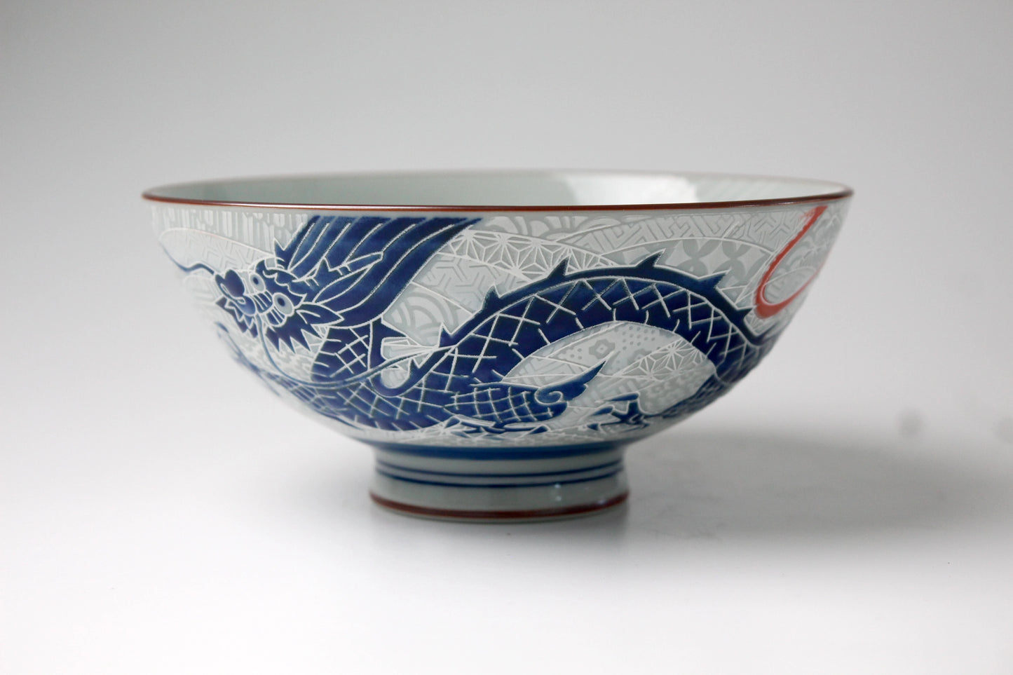 A handcrafted porcelain rice bowl with an intricately etched blue dragon on the exterior and a printed dragon inside, featuring a glossy finish and detailed artistry.