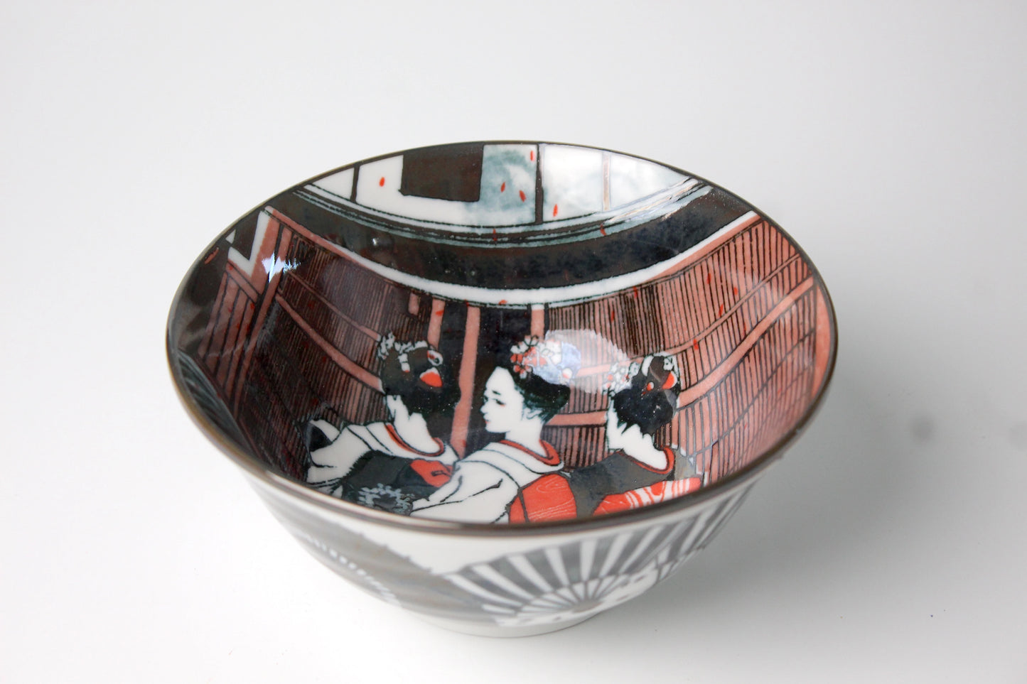 Japanese porcelain rice or ramen bowl featuring an intricate design of geisha in traditional attire, accented with red and black details.