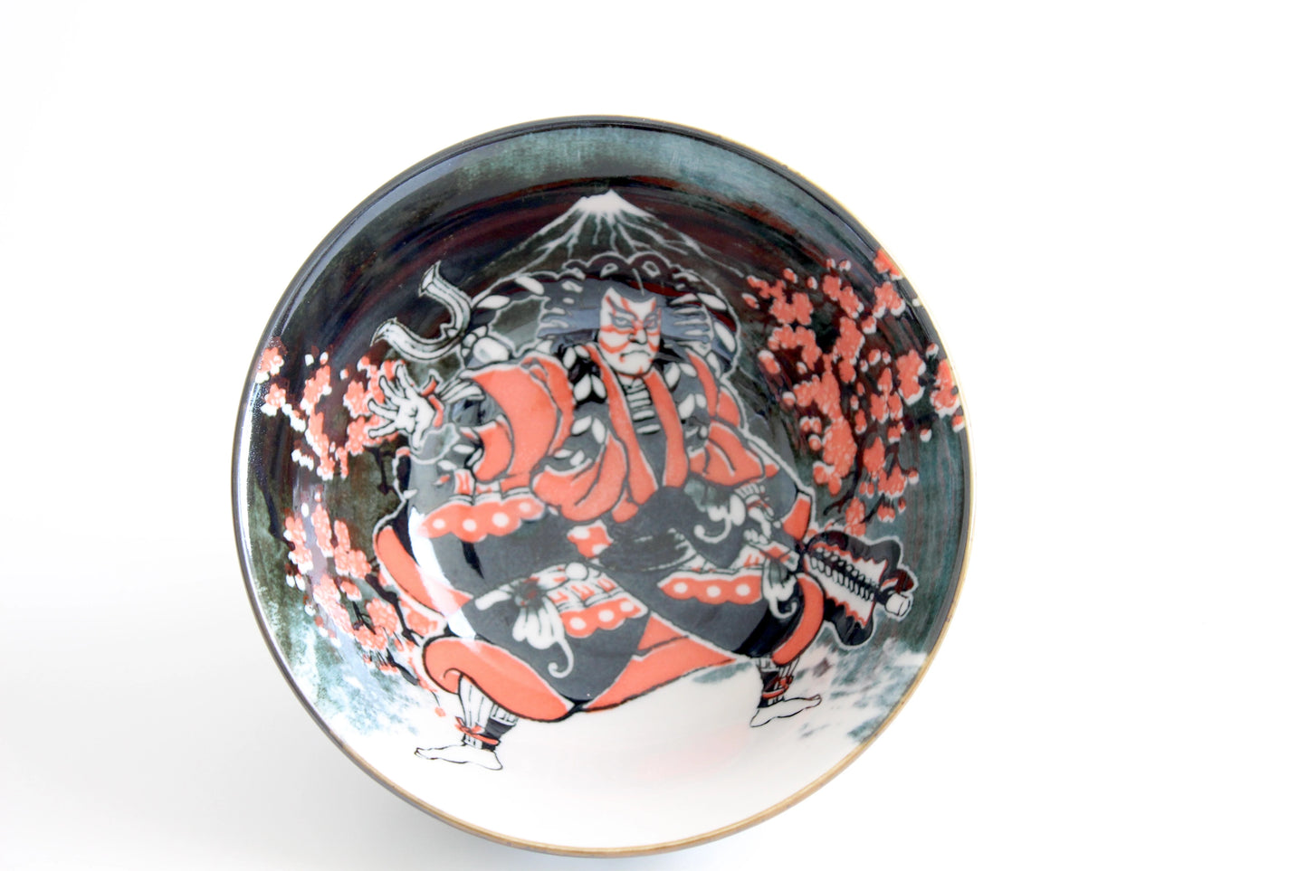 Overhead view of a ceramic ramen bowl featuring a kabuki actor in red costume, Mt. Fuji in the background, and pink cherry blossoms.
