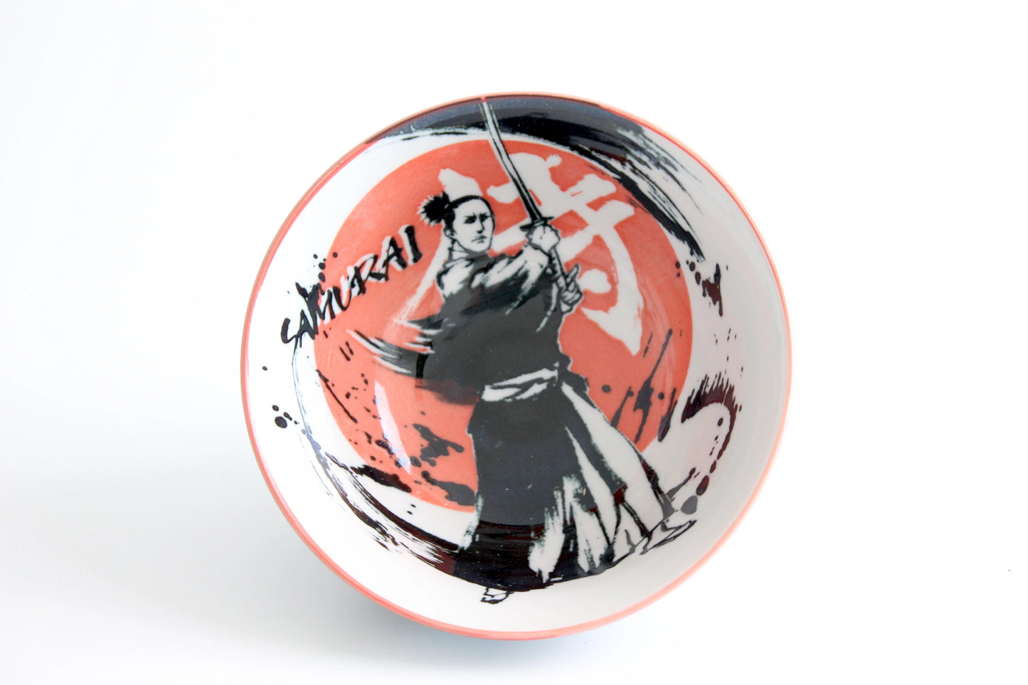 Overhead view of a ceramic ramen bowl featuring a black brushstroke samurai design and the word “Samurai” on a red swirl background.