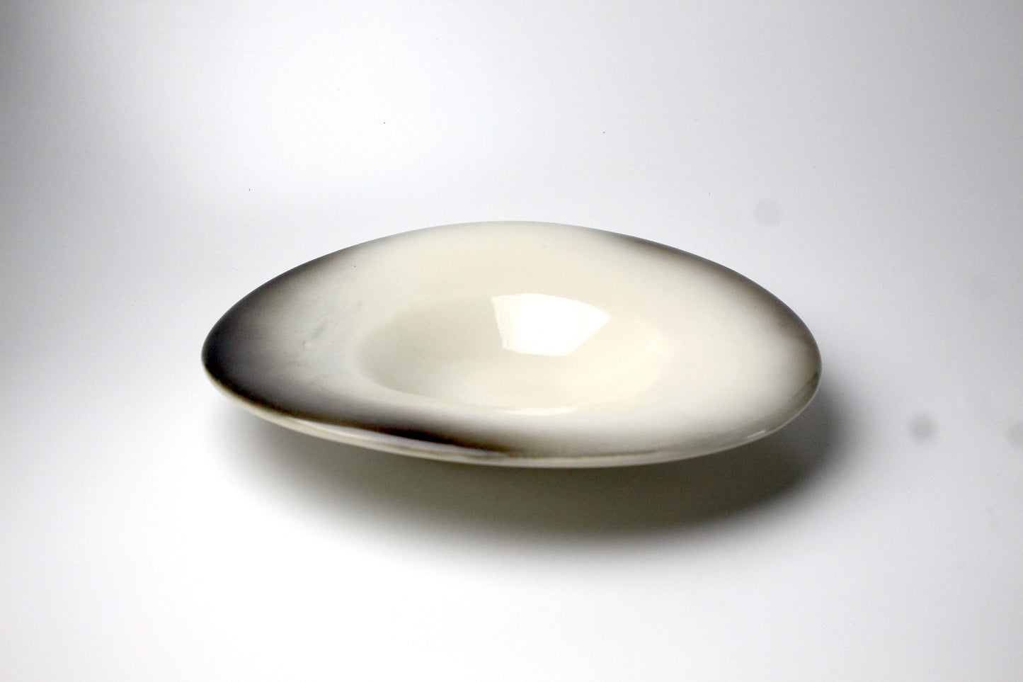 A handcrafted shallow ceramic plate with a glossy finish, featuring a smooth gradient glaze transitioning from ivory to deep earthy tones.