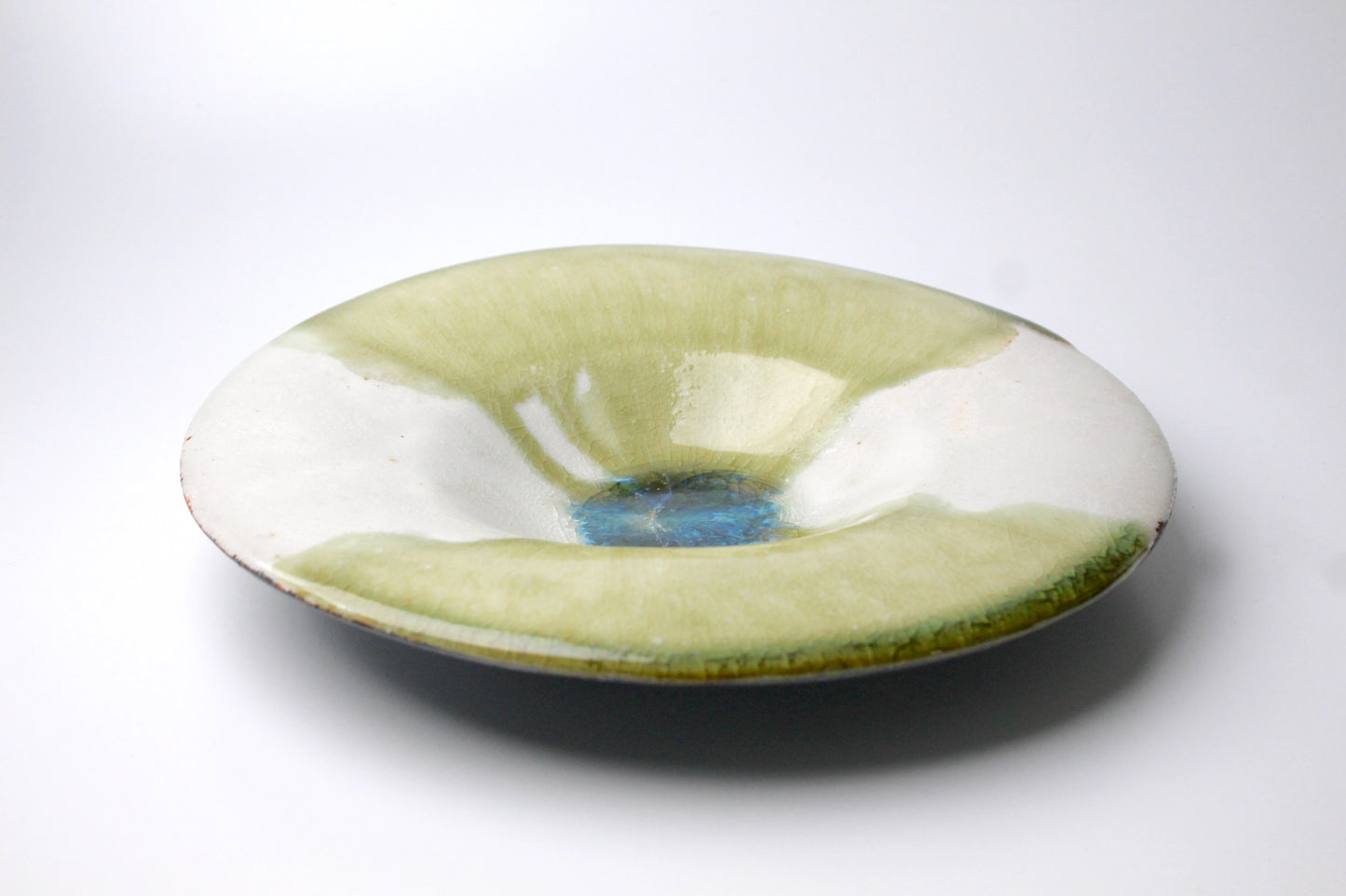 A shallow ceramic plate with a glossy glaze, featuring a blend of green, white, and blue hues with an artistic, organic texture.