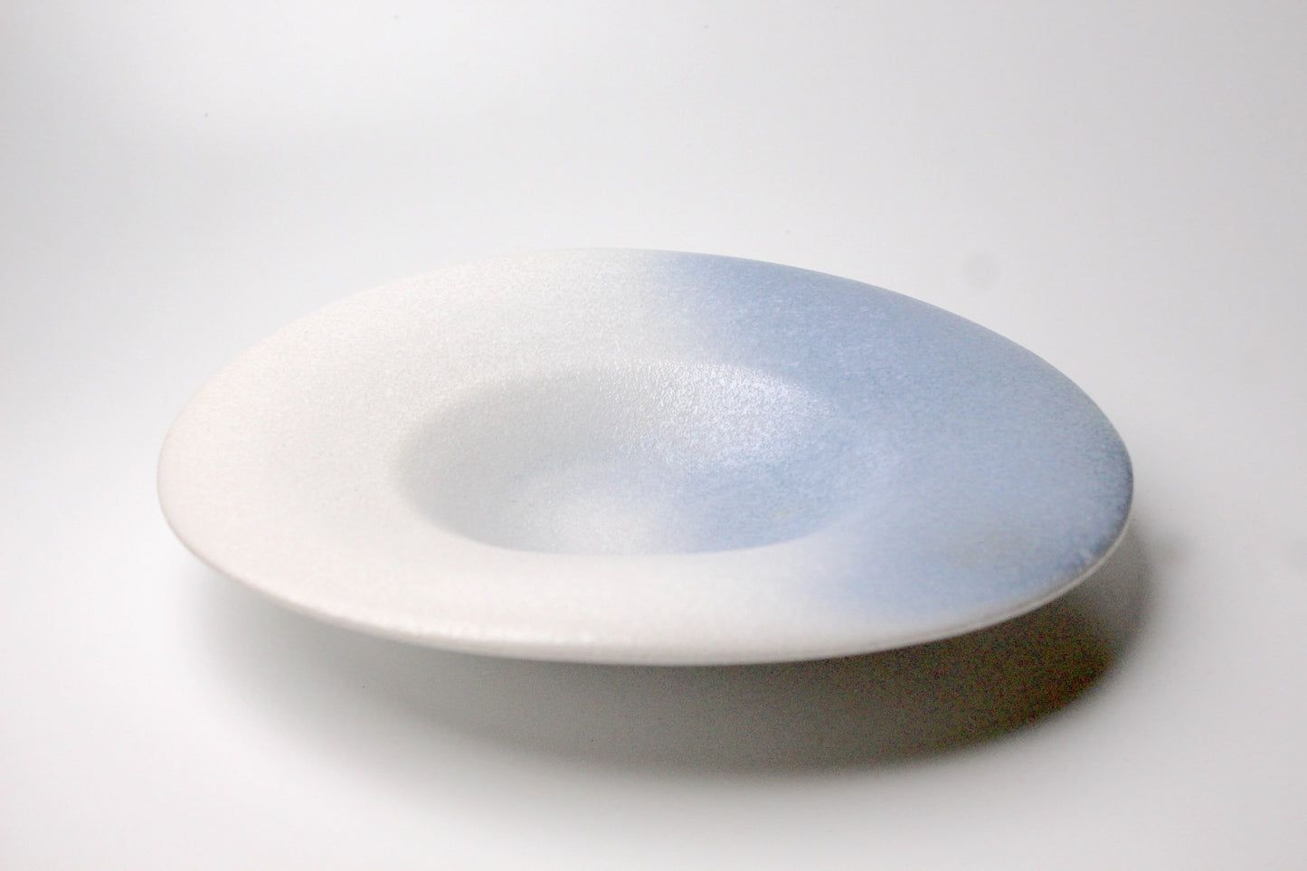 A ceramic plate with a matte finish, featuring a smooth gradient of white and soft blue, designed with a minimalist aesthetic