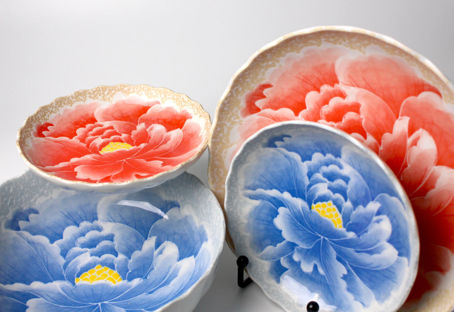 A stunning dinnerware set featuring intricate hand-painted peony motifs in vibrant red and blue, with a high-gloss finish, perfect for elegant dining and special occasions.