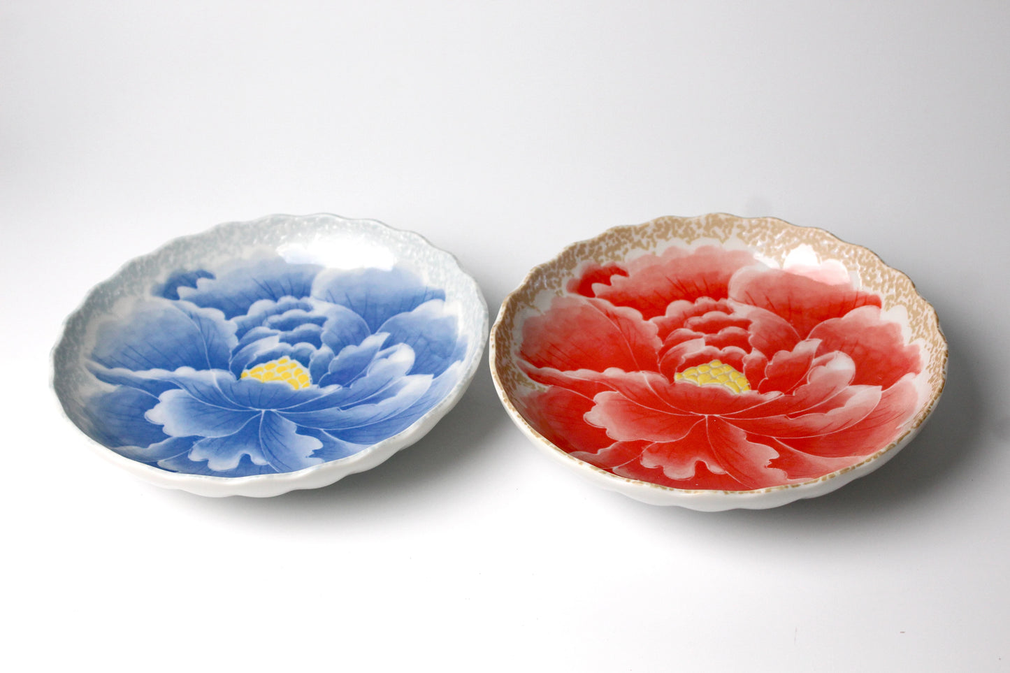 A pair of exquisite ceramic plates featuring hand-painted peony flower motifs in vibrant red and blue, finished with a glossy glaze and intricate detailing for an elegant dining experience.