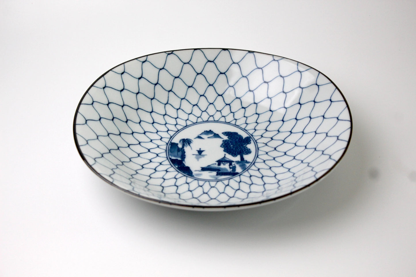 A Japanese porcelain plate in Saikai style, featuring a medallion with mountains and sea. Surrounded by a lattice.