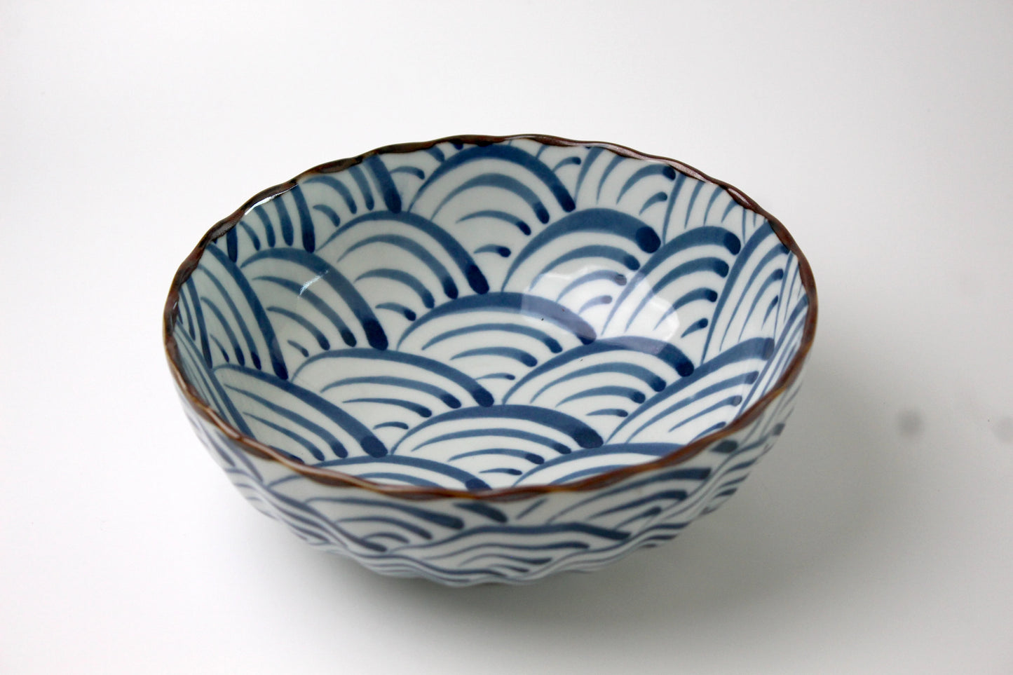 A Japanese ceramic bowl featuring waves of the blue sea pattern in deep blue, with a scalloped rim and a glossy finish.