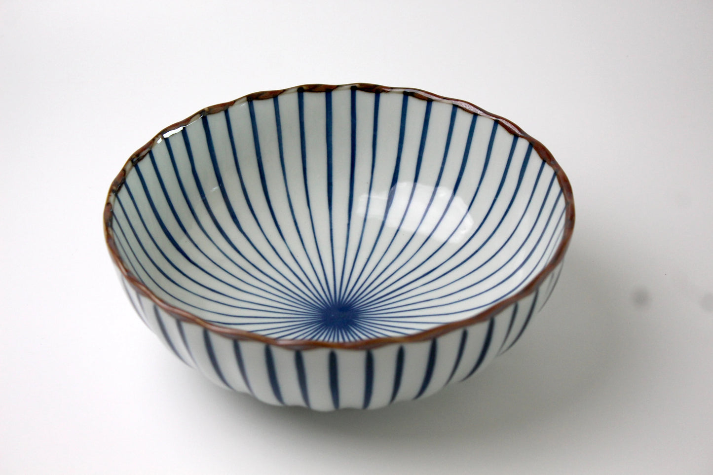 A Japanese ceramic bowl featuring a delicate radial Sensu (fan) pattern in deep blue, with a scalloped rim and a glossy finish.