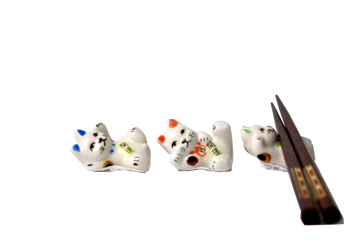 Three ceramic Maneki Neko spoon rests in playful poses, each featuring different ear and collar colors—blue, orange, and green. These lucky cat spoon rests are designed to hold chopsticks or utensils, adding a charming and functional touch to any dining setup.