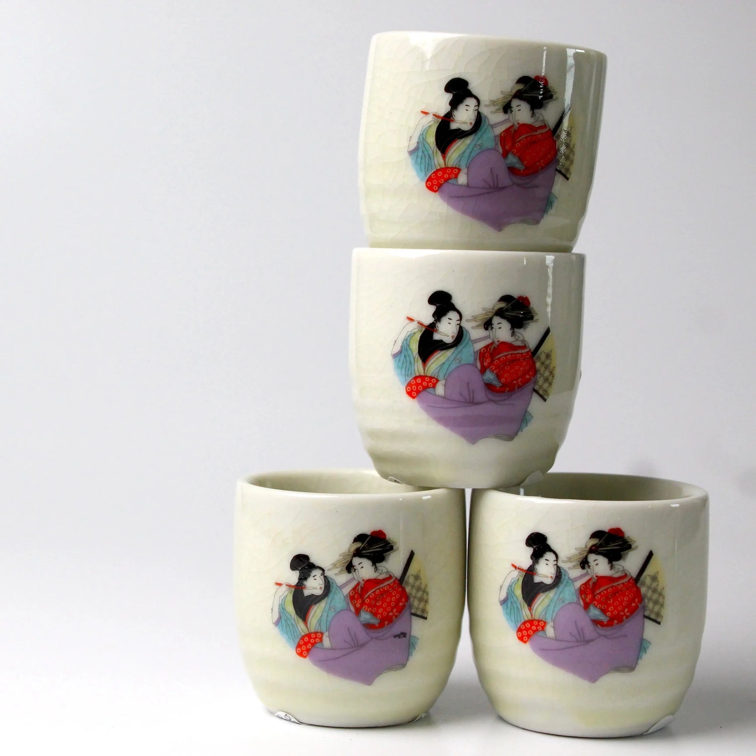 Four stacked cream colored sake cups with Heian women imprinted on the outside