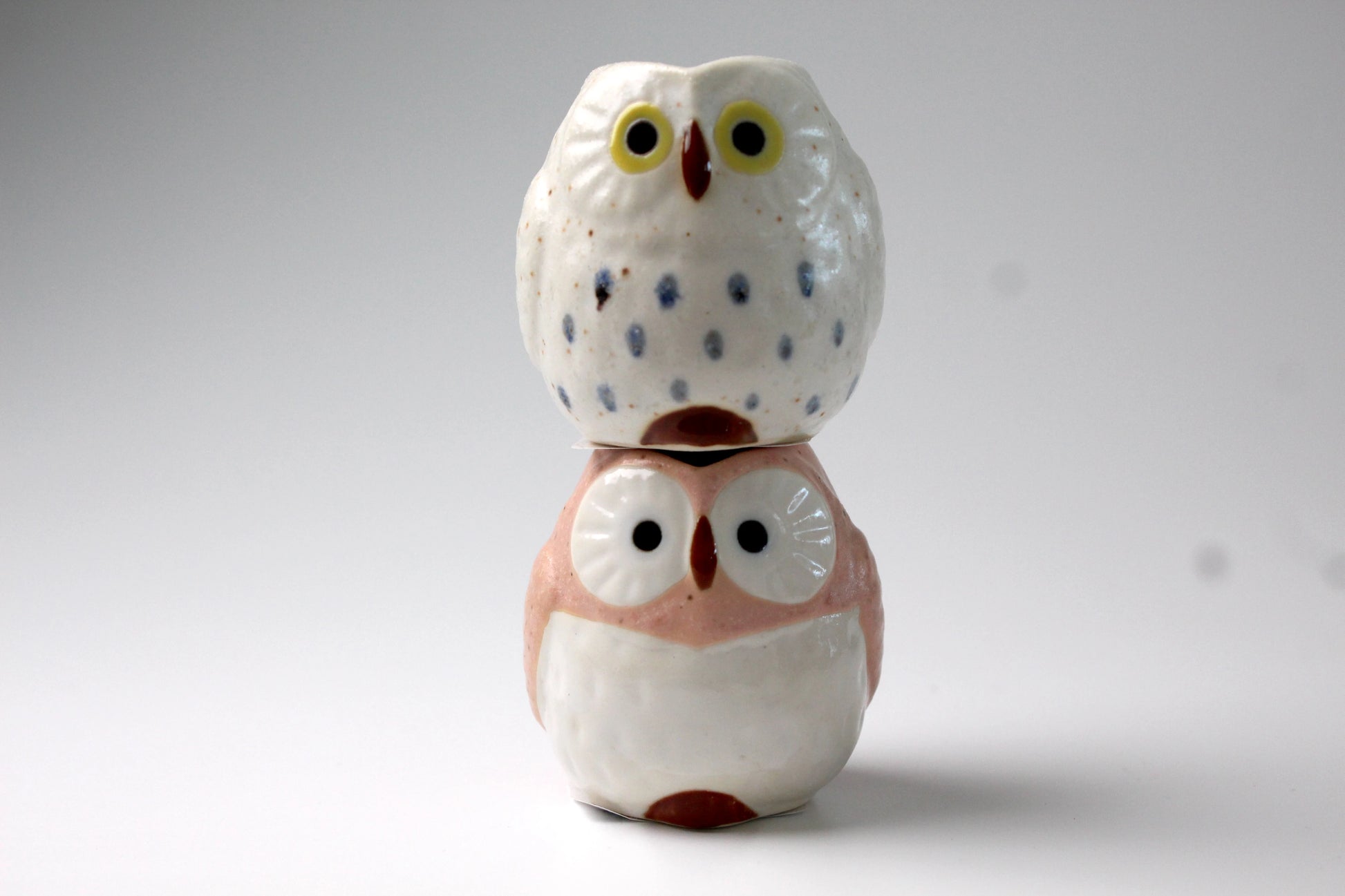 White & pink ceramic owls shaped milk pitchers. The owls are sitting on top of each other.