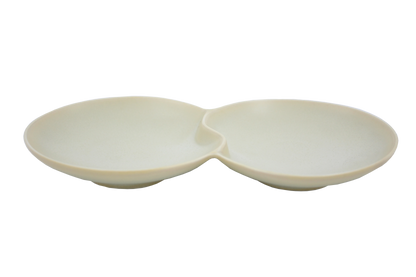 An isometric view of the Missera Hotate, a cream ceramic divided serving dish with two circular sections joined in the center like a clam shell. Perfect as a multi compartment serving dish for snacks and dips.