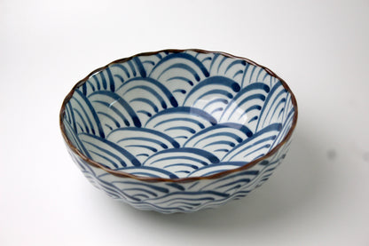 A Japanese ceramic bowl featuring waves of the blue sea pattern in deep blue, with a scalloped rim and a glossy finish.