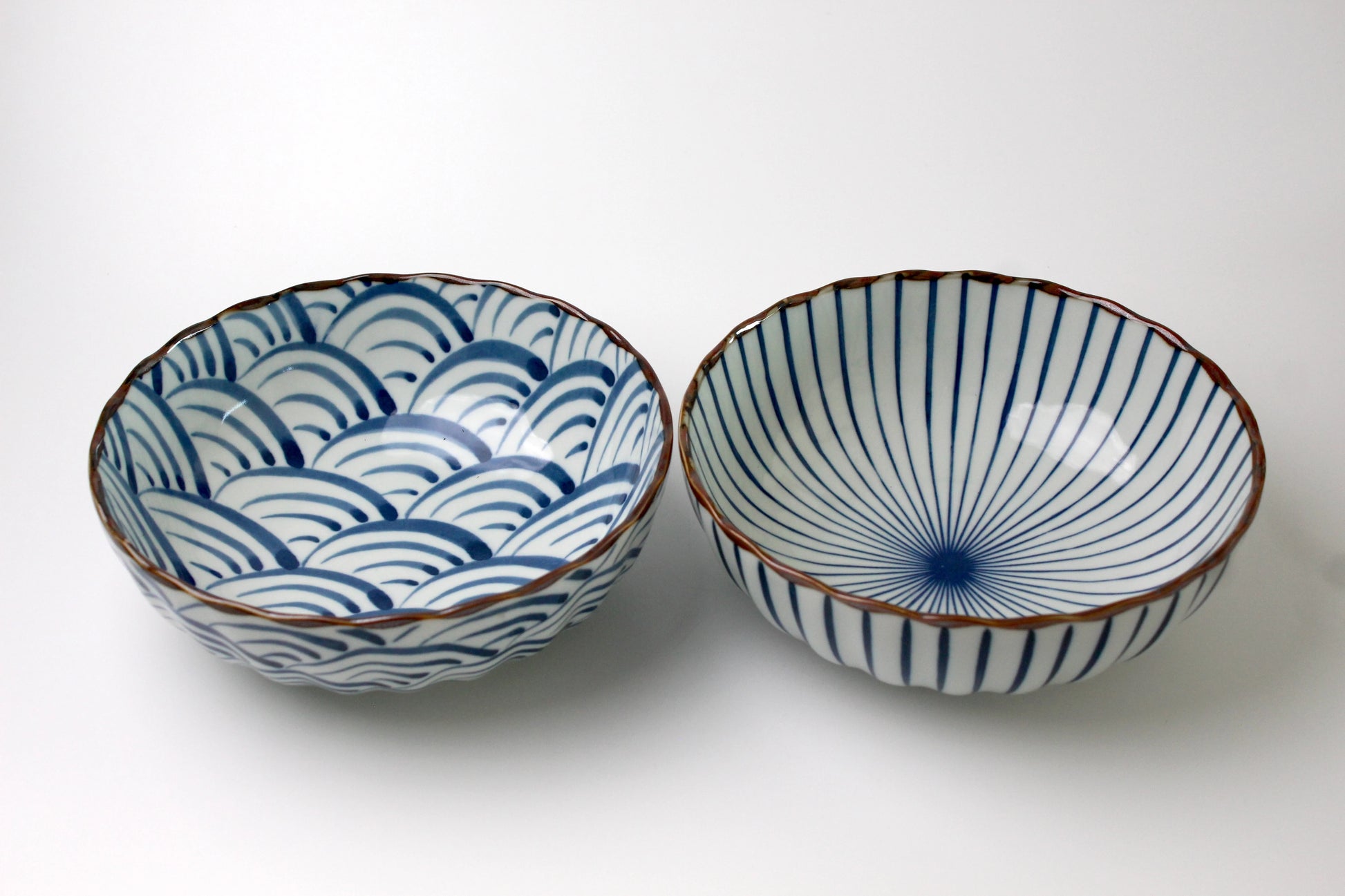 A pair of Japanese ceramic bowls featuring traditional Seigaiha (blue ocean waves) and Sensu (fan) patterns with a scalloped rim and a glossy finish.