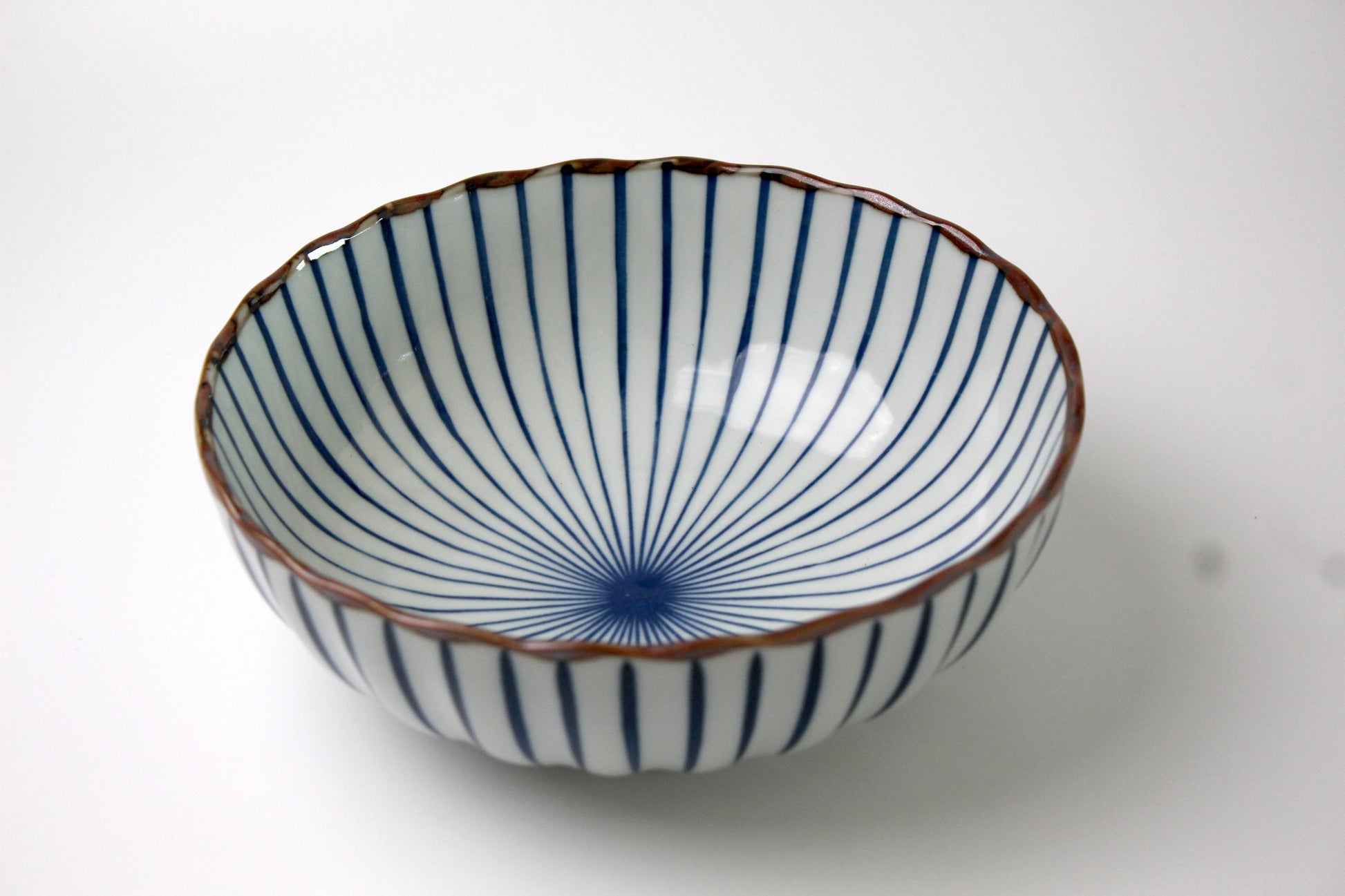 A Japanese ceramic bowl featuring a delicate radial Sensu (fan) pattern in deep blue, with a scalloped rim and a glossy finish.